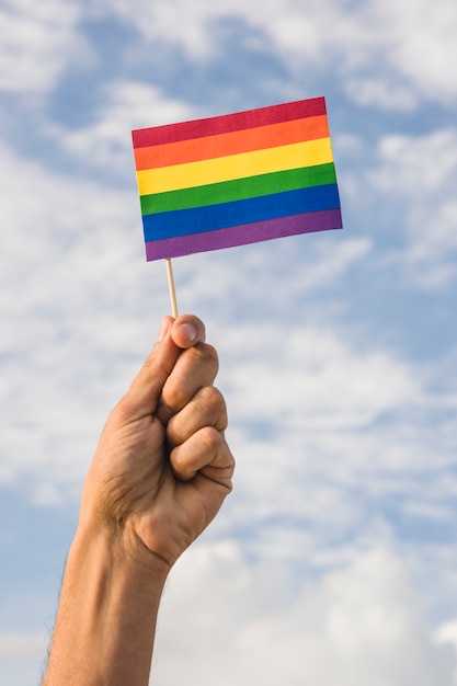 Hombre que sostiene la bandera en colores LGBT y cielo azul