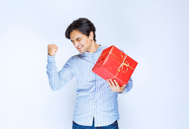 Hombre que sostiene una caja de regalo roja y se siente exitoso. Foto de alta calidad