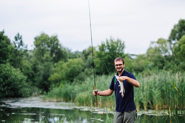 Hombre que sostiene la caña de pescar con pescado en el gancho