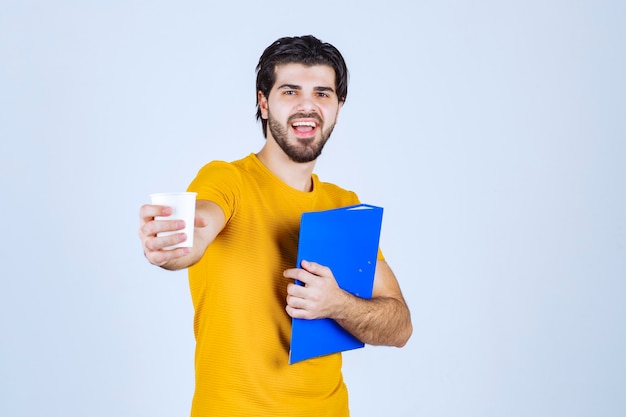 Hombre que sostiene una carpeta azul y una taza de café.