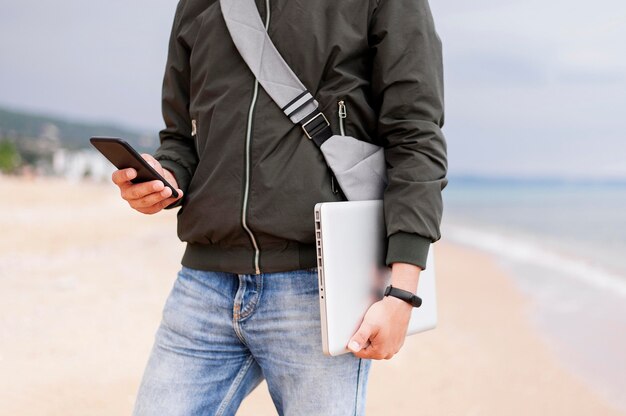 Hombre que sostiene la computadora portátil y el teléfono inteligente en la playa