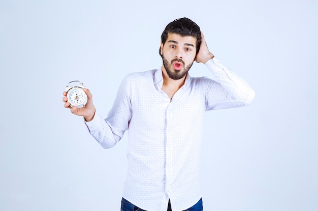 Hombre que sostiene un despertador y confundido porque llega tarde