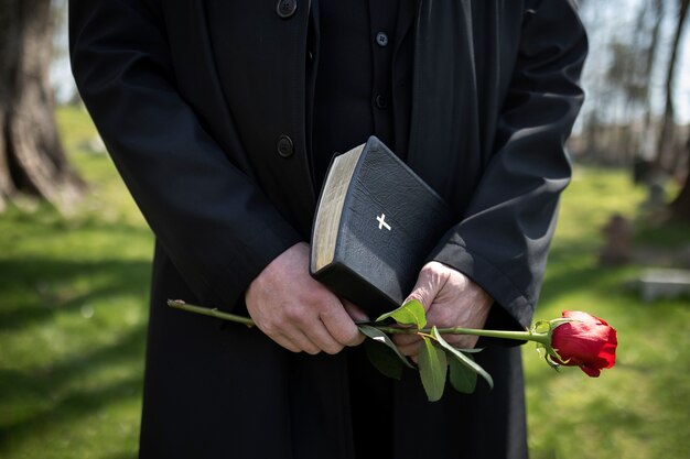 Hombre que sostiene flores y biblia en el cementerio