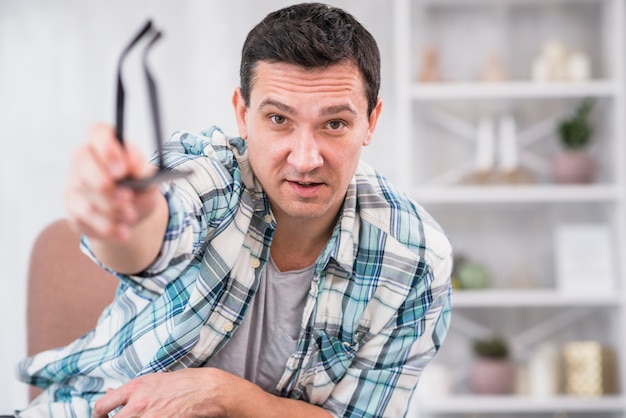 Foto gratuita el hombre que sostiene las lentes en estiró la mano en silla en casa