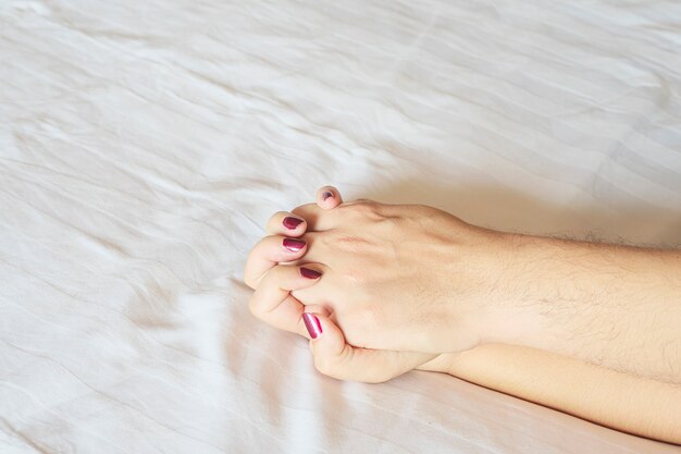 Hombre que sostiene la mano de la mujer en la cama blanca, pareja concepto sexual