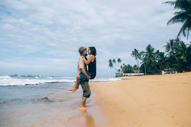 Hombre que sostiene a novia y que se besa en la playa