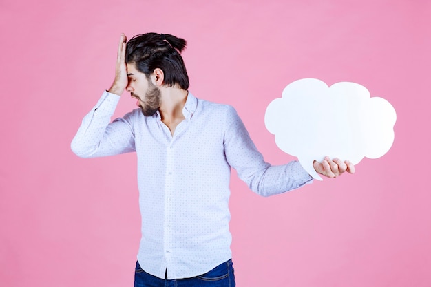 Foto gratuita hombre que sostiene un panel de ideas en forma de nube y parece insatisfecho.