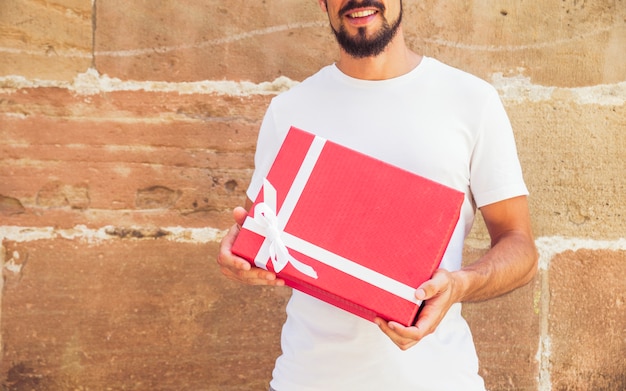 Hombre que sostiene el regalo delante de fondo de la pared