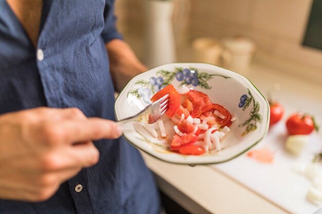 Hombre que sostiene la rodaja de tomate con un tenedor en el cuenco