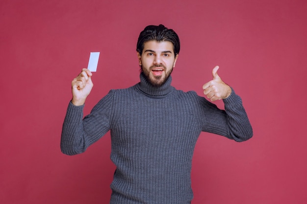 Hombre que sostiene su tarjeta de visita y hace un signo de mano positivo.