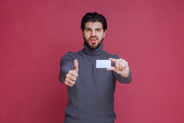 Hombre que sostiene su tarjeta de visita y hace un signo de mano positivo.