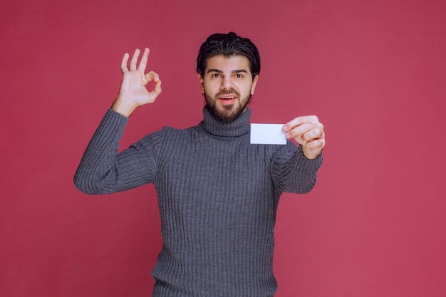 Hombre que sostiene su tarjeta de visita y hace un signo de mano positivo.