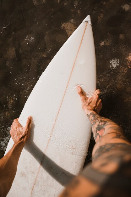 Hombre que sostiene la tabla de surf en el agua cerca de la costa