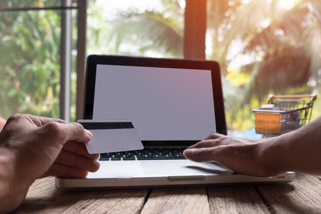 Hombre que sostiene la tarjeta de crédito en la mano y que incorpora el código de seguridad usando el teclado del ordenador portátil