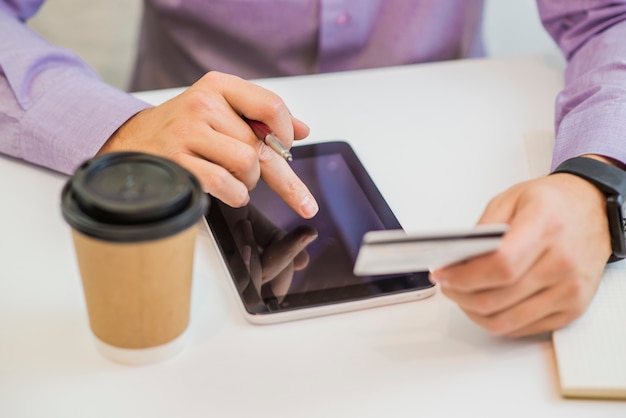 Hombre que sostiene la tarjeta de crédito y la tableta en fondo del lugar de trabajo