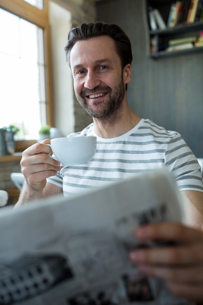 Hombre que sostiene una taza de café y leyendo el periódico en la cafetería