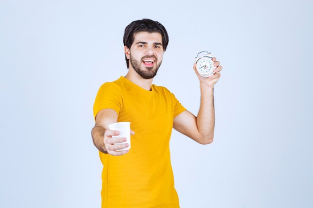 Hombre que sostiene una taza de café y un reloj despertador que apunta a la rutina matutina.