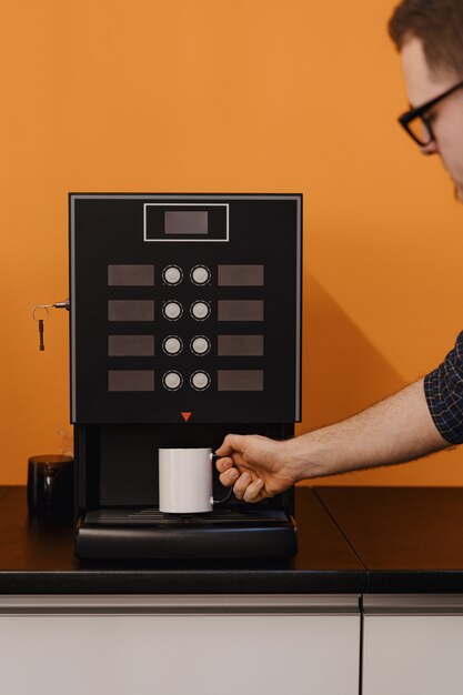 Un hombre que sostiene una taza cerca de una máquina de café negro