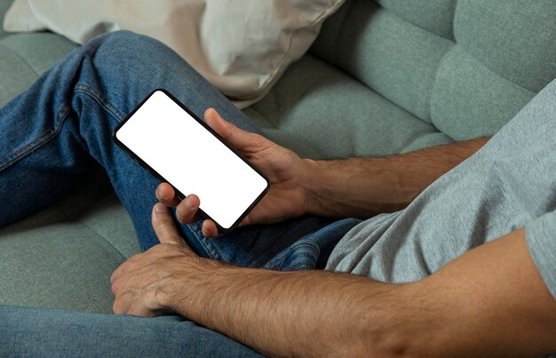 Hombre que sostiene el teléfono inteligente mientras está sentado en el sofá