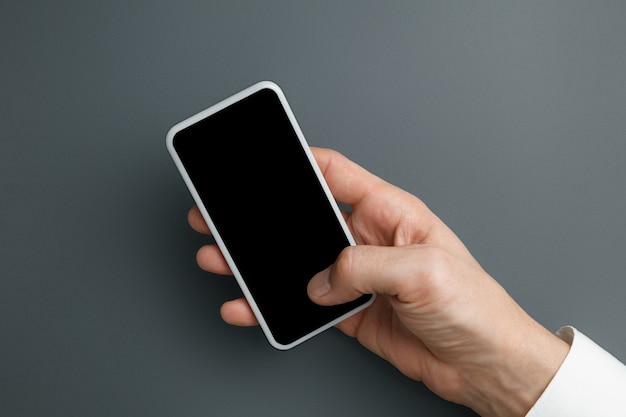 Hombre que sostiene el teléfono inteligente con pantalla vacía en la pared gris para texto o diseño.