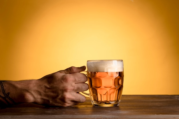 Hombre que sostiene el vaso de cerveza en la mesa de madera