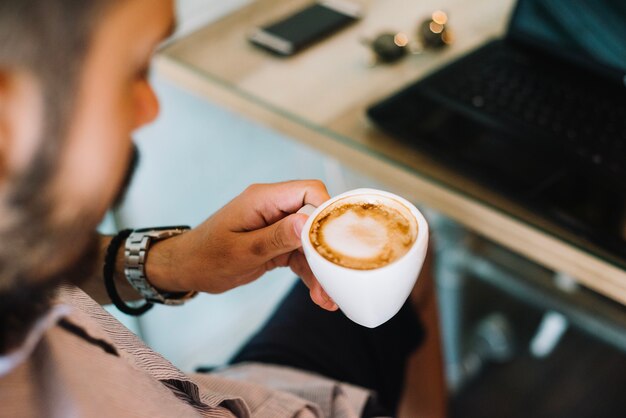 Hombre que tiene capuchino en la computadora portátil