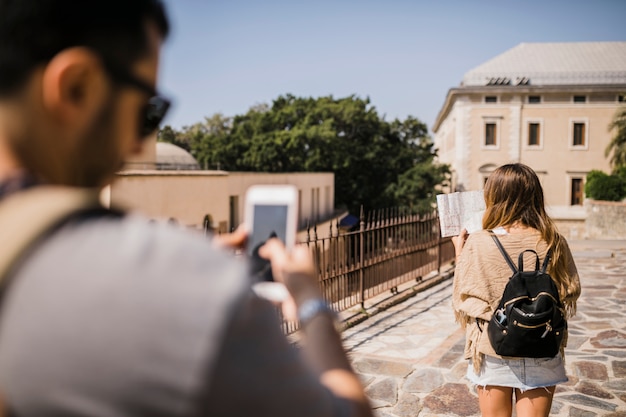 Hombre que toma la fotografía de una mujer mirando el mapa de pie en la calle