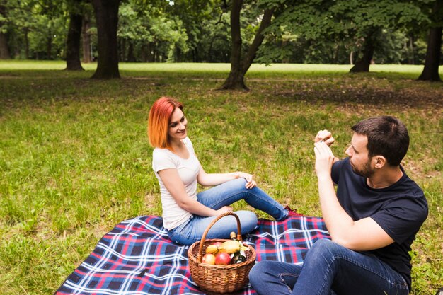 Hombre que toma la fotografía de su novia en el teléfono celular en picnic