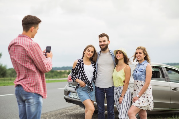 Hombre que toma la imagen de sus amigos que se colocan delante del coche en el camino