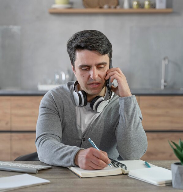 Hombre que trabaja en el campo de los medios de comunicación con una llamada telefónica y escribiendo cosas en el cuaderno