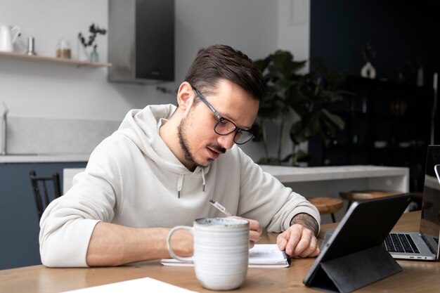 Hombre que trabaja desde casa en el escritorio en la tableta y la escritura