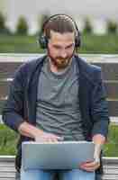 Foto gratuita hombre que trabaja en la computadora portátil con auriculares al aire libre