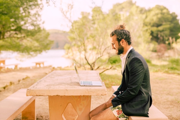 Hombre que trabaja con la computadora portátil en el parque soleado