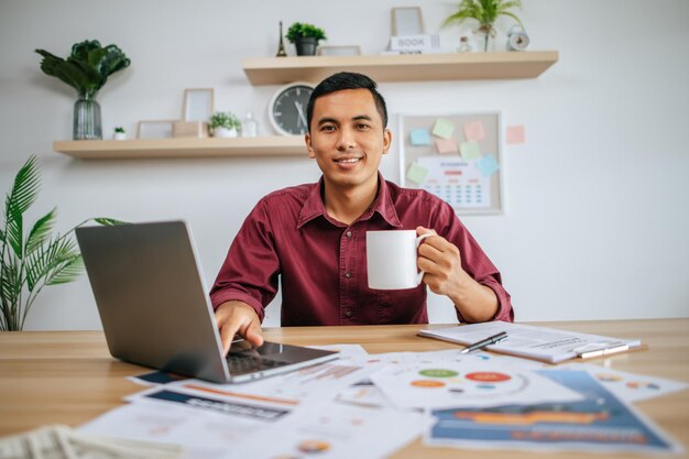 Hombre que trabaja con la computadora portátil y sosteniendo la taza de café