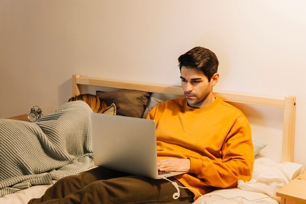 Hombre que usa la computadora portátil en cama cerca de esposa