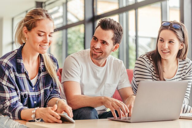 Hombre que usa la computadora portátil que se sienta entre las mujeres