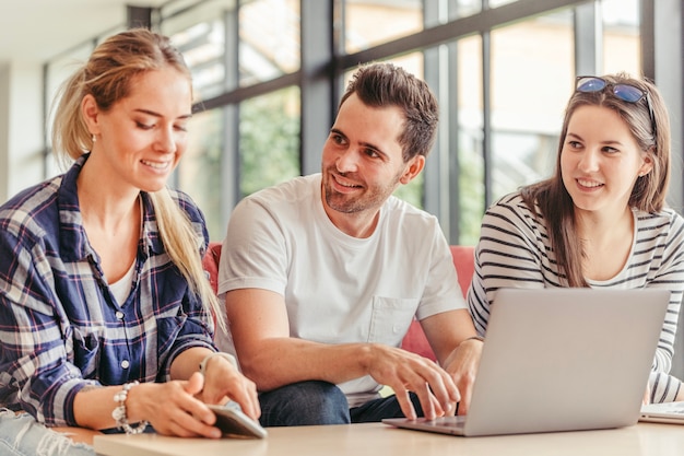 Hombre que usa la computadora portátil que se sienta entre las mujeres