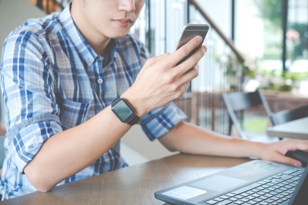 Hombre que usa el smartphone con la computadora portátil en la cafetería del café