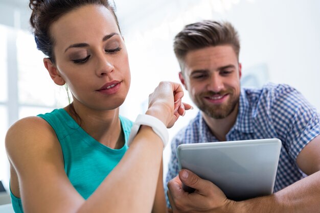 Hombre que usa la tableta digital, mientras que la mujer que controla el tiempo en su reloj de pulsera