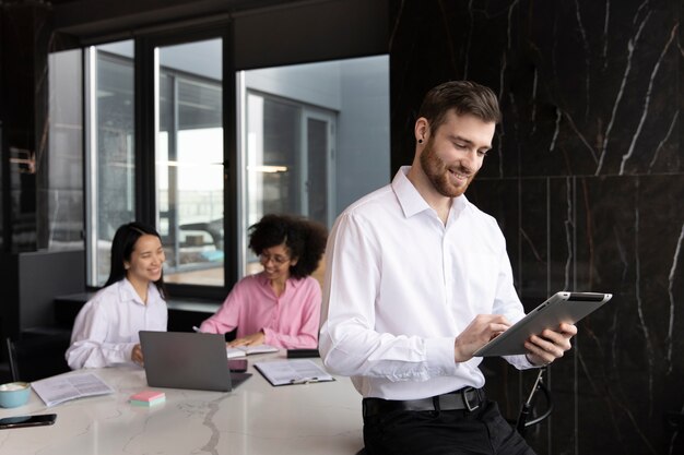 Hombre que usa una tableta para trabajar mientras sus colegas femeninas usan una computadora portátil