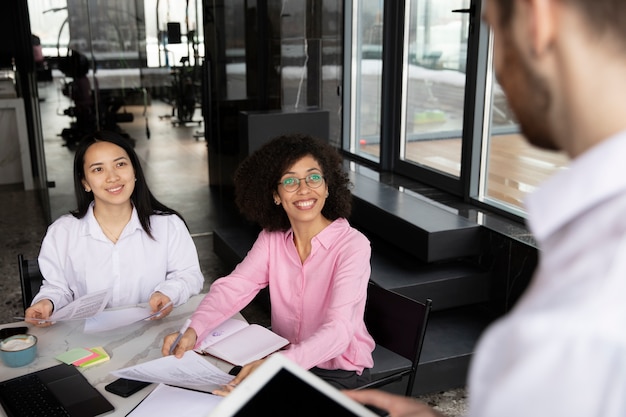 Foto gratuita hombre que usa una tableta para trabajar mientras sus colegas femeninas usan una computadora portátil