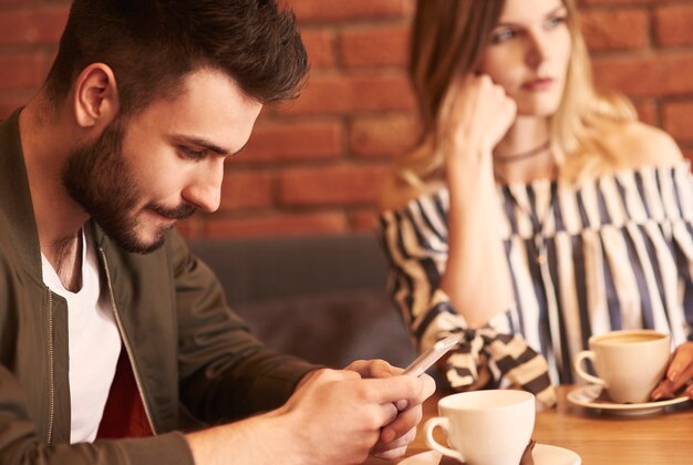 Hombre que usa el teléfono celular durante la reunión con su novia