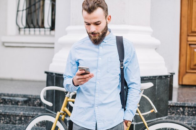 Hombre que usa el teléfono inteligente cerca de la bicicleta