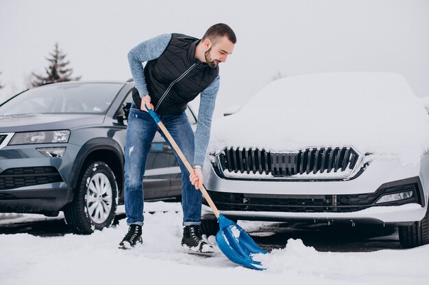 Hombre quitando nieve con pala por el coche