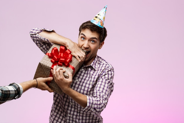 Hombre rasgando regalo de cumpleaños en caja sobre pared púrpura.