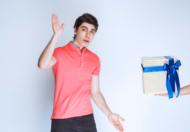 Hombre recibiendo y sosteniendo una caja de regalo blanca envuelta con cinta azul con ambas manos