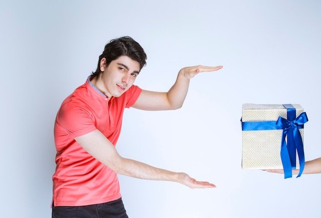 Hombre recibiendo y sosteniendo una caja de regalo blanca envuelta con cinta azul con ambas manos