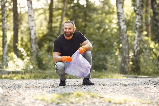 Hombre recoge basura en bolsas de basura en el parque