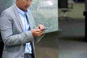 Foto gratuita hombre recortado leyendo mensajes de texto en su teléfono inteligente de pie en el edificio de oficinas