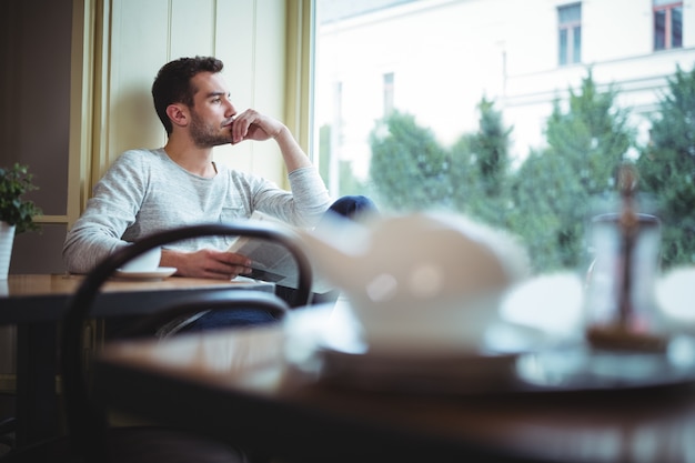 Hombre reflexivo mirando por la ventana, mientras que la lectura de periódicos